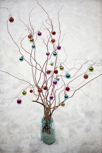 small branches or twigs in a bottle with pompoms and ornaments